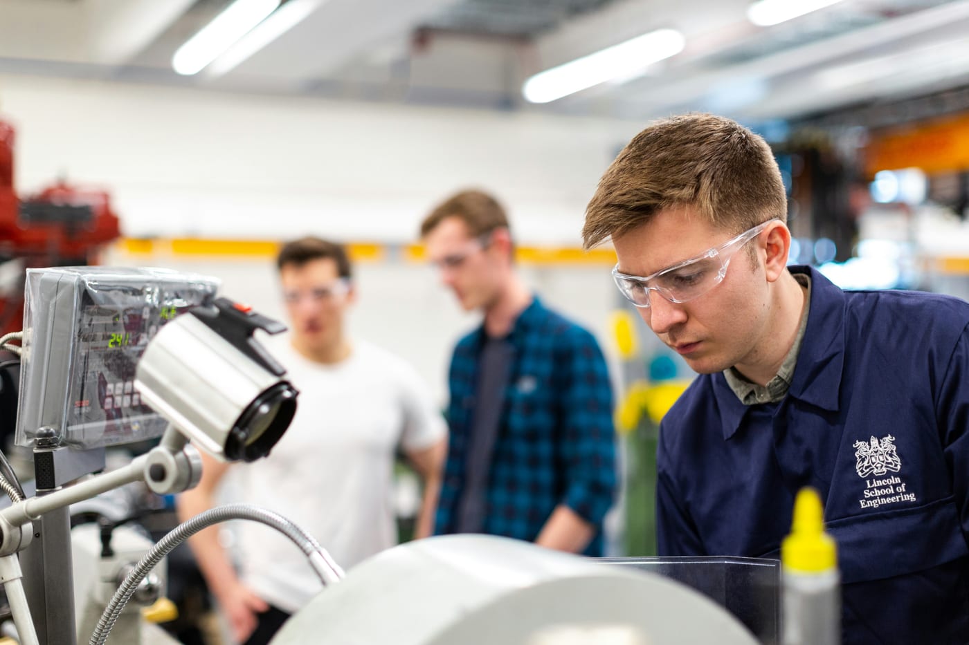 Junge Ingenieure mit Schutzbrillen an einem Messaufbau in der Werkstatt – förderfähige Entwicklungsarbeit im Unternehmen